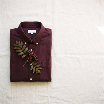 Folded deep burgundy oxford shirt on cream linen