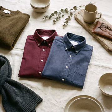 Two folded oxford shirts in burgundy and navy on cream linen
