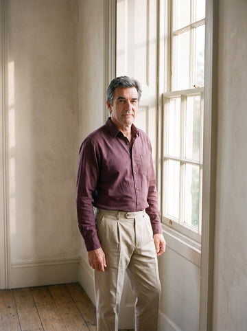 Man in a burgundy oxford shirt beside a tall window in autumn light