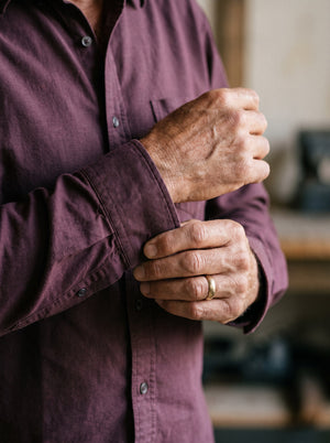 Hands turning back the cuff of a burgundy oxford shirt